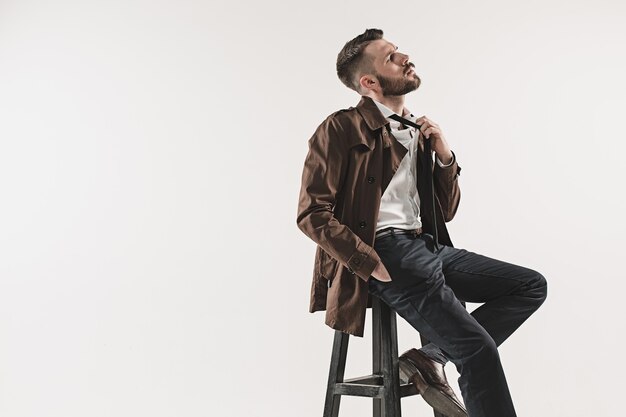 Portrait of stylish handsome young man sitting at studio against white. Man wearing jacket