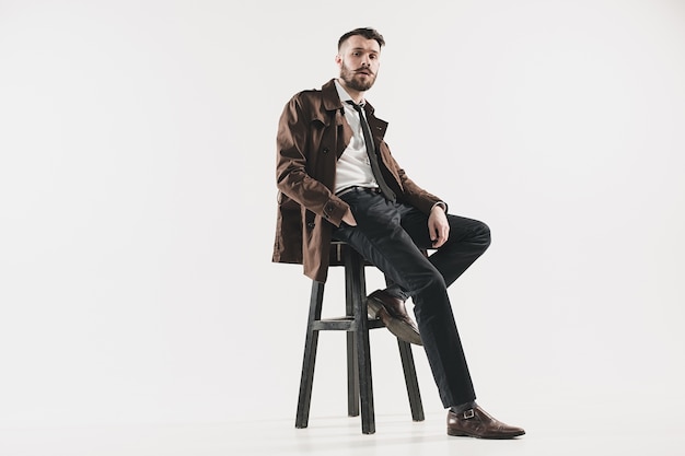 Portrait of stylish handsome young man sitting at studio against white. Man wearing jacket