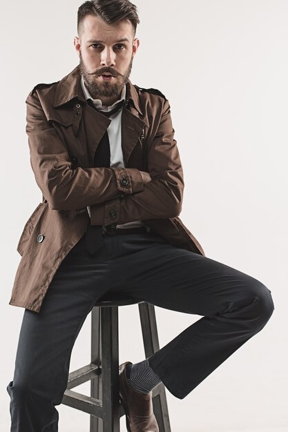 Portrait of stylish handsome young man sitting at studio against white. Man wearing jacket
