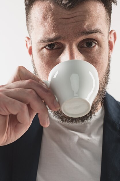 Portrait of stylish handsome young man standing at studio. Man wearing jacket and holding cup of coffee