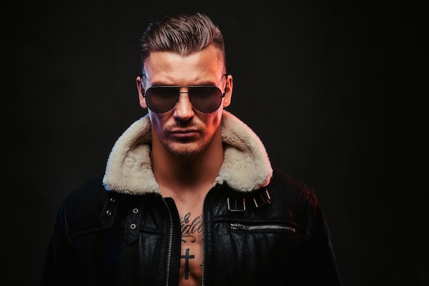 Portrait of a stylish man in jeans jacket with dark glasses and stylish hair on a dark background.