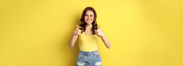 Free photo portrait of stylish modern girl feminine woman showing thumbs up recommending gesture like or approv
