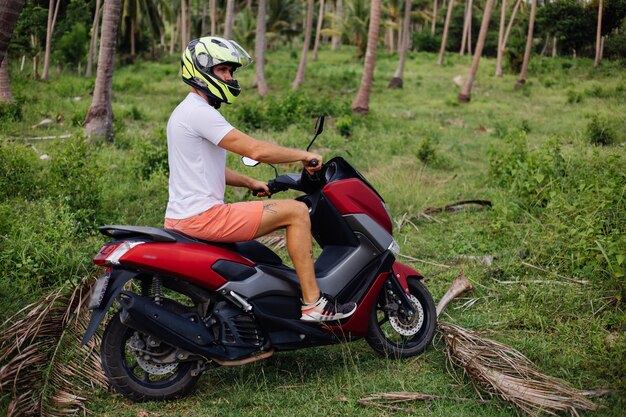 Portrait of stylish tattooed male tourist in sunglasses, helmet and blue open shirt on motorbike