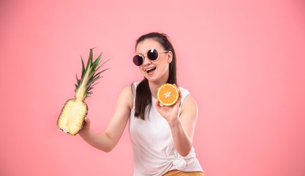 portrait of a stylish woman on a pink background with fruit in her hands. Summer concept.