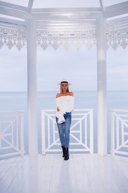Portrait of stylish woman in voluminous white trendy top and classic luxury hat under carved arch