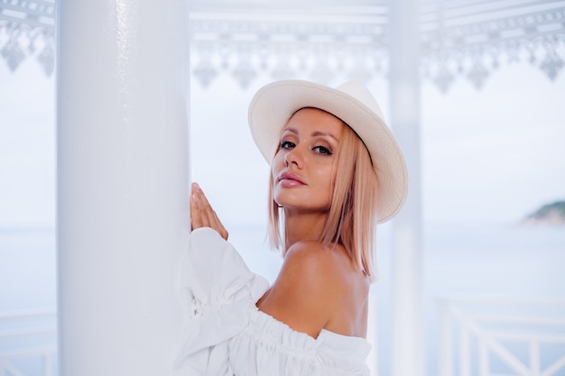 Portrait of stylish woman in voluminous white trendy top and classic luxury hat
