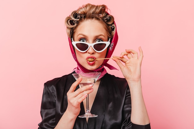 Free photo portrait of stylish woman with curlers, dressed in black dress eating olive