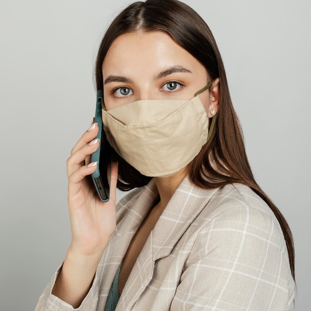 Donna alla moda del ritratto con la maschera facendo uso del cellulare