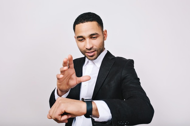 Portrait stylish young man in white shirt, black jacket having fun with watch on white background. Magic time, smart worker, successful businessman, meeting, work, joy