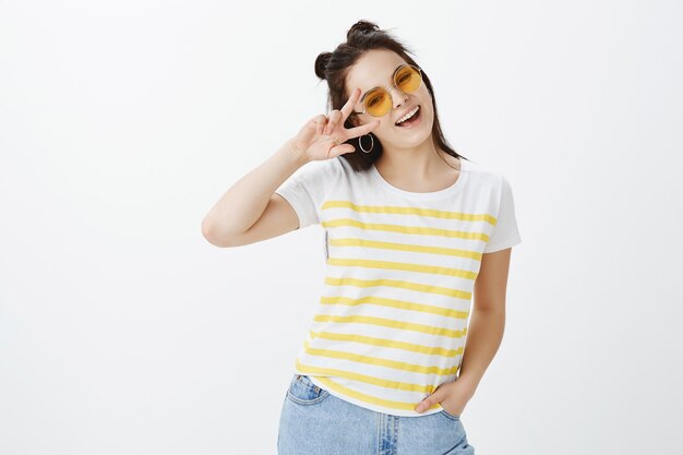 Portrait of stylish young woman posing with sunglasses against white wall