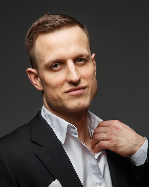 Portrait of successful business man in a black suit on grey background.