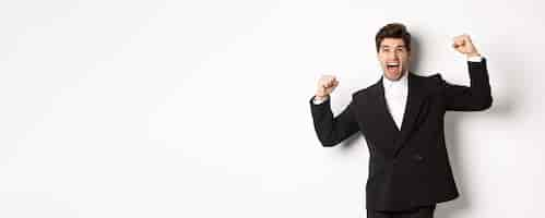 Free photo portrait of successful businessman in black suit become champion raising hands up and shouting yes t