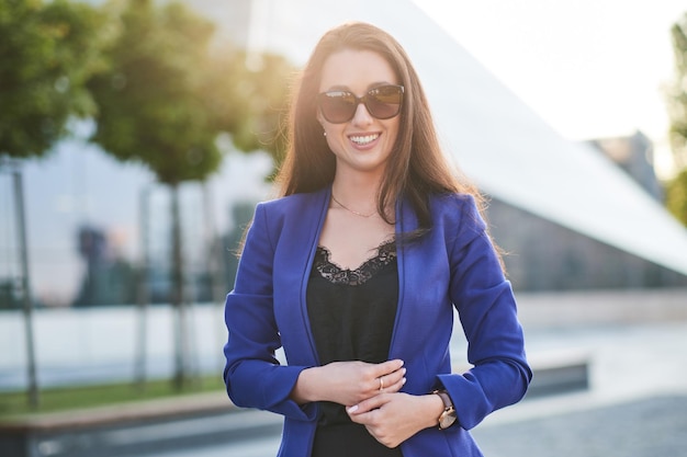 Foto gratuita ritratto di una donna d'affari di successo con un sorriso affascinante in posa per strada con un'architettura interessante sullo sfondo.