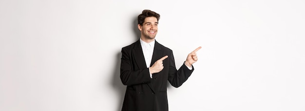 Portrait of successful handsome man in suit pointing and looking left with pleased smile showing pro