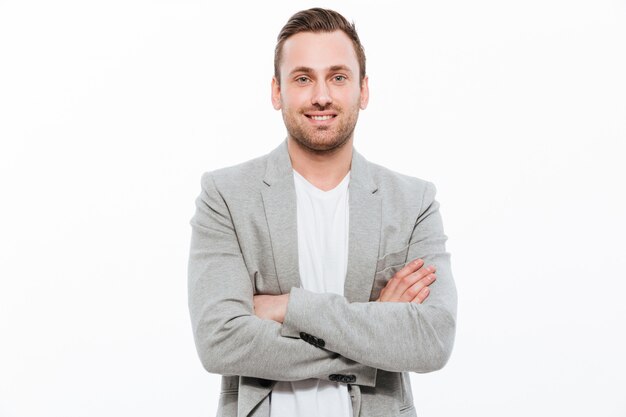 Portrait of successful man having stubble posing with broad smile keeping arms folded