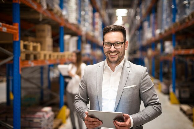 Portrait of successful middle aged manager businessman holding tablet computer in large warehouse organizing distribution