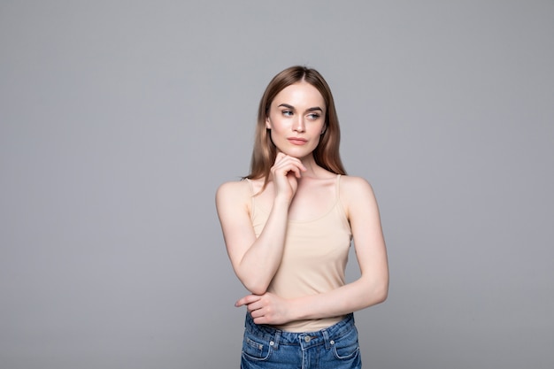 Free photo portrait of successful woman looking aside and holding finger at cheek while smiling isolated over gray wall