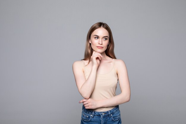 Portrait of successful woman looking aside and holding finger at cheek while smiling isolated over gray wall