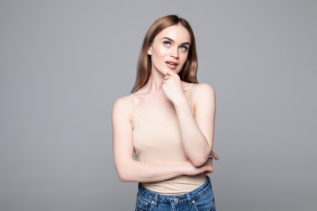 Free photo portrait of successful woman looking aside and holding finger at cheek while smiling isolated over gray wall