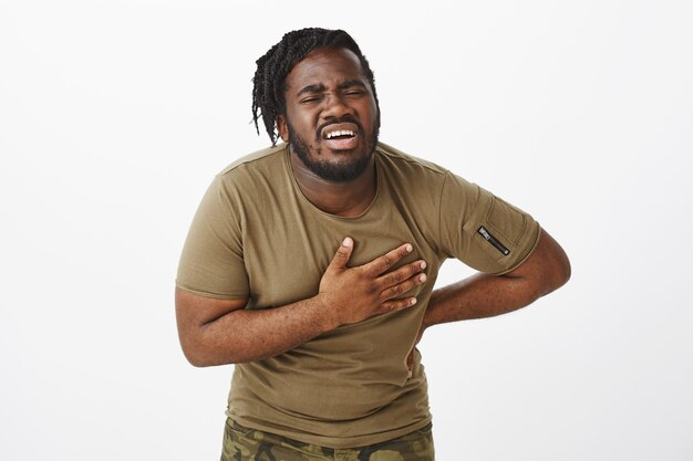 Portrait of suffering guy in a brown t-shirt posing against the white wall