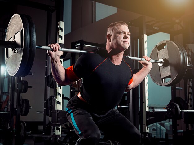 Portrait of super fit muscular young man working out in gym with barbell