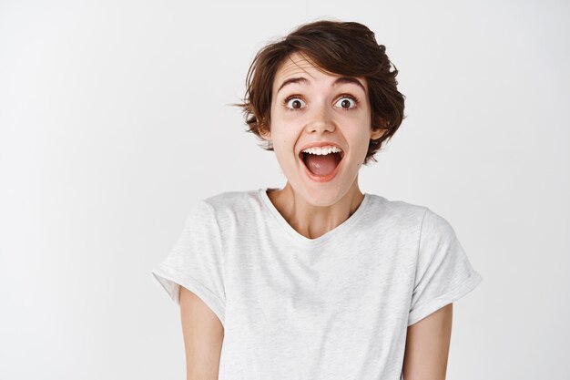 Portrait of surprised and amused caucasian woman, drop jaw and looking amazed , white wall