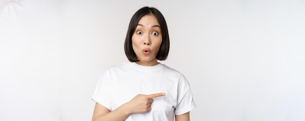 Portrait of surprised asian woman say wow pointing right at amazing product offer sale or logo standing over white background