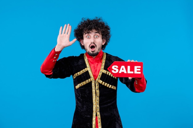 Free photo portrait of surprised azeri man in traditional costume holding sale nameplate on blue background shopping spring ethnic novruz