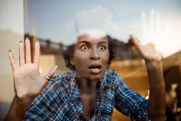 Portrait of surprised beautiful african behind glass playing ape. Shot from outside.