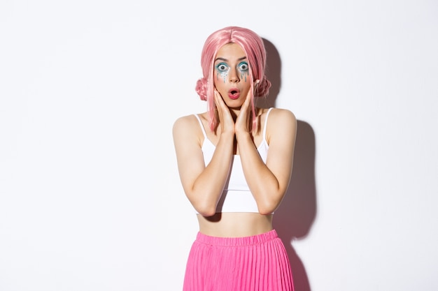 Portrait of surprised caucasian girl in pink wig and bright makeup, gasping amazed and stare at camera