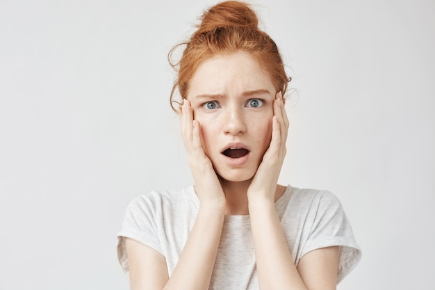 Portrait of surprised displeased freckled woman with hands on cheeks