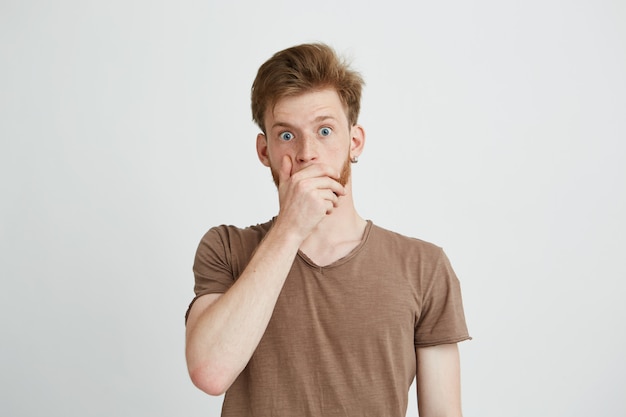 Portrait of surprised frightened scared young man closing mouth with hands.