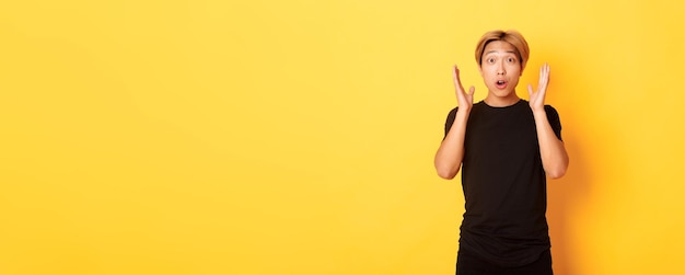 Portrait of surprised gasping blond asian guy reacting to awesome news yellow background