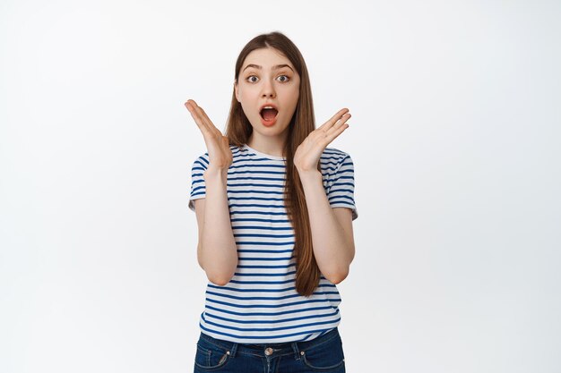 Portrait of surprised girl stare amazed at camera, gasping and say wow impressed, standing over white background