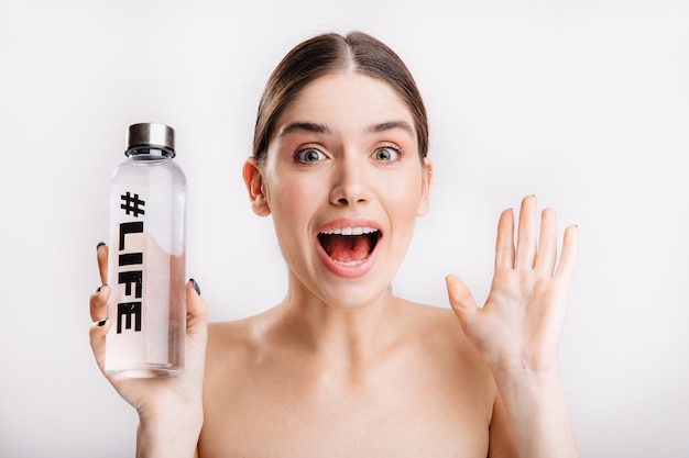 Portrait of surprised girl with clean healthy skin. Lady posing in surprise, holding bottle of water with inscription life on it.