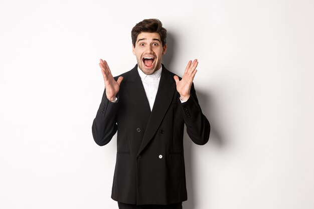 Portrait of surprised handsome businessman in suit, reacting to holidays promo, looking amazed at camera, standing over white background.