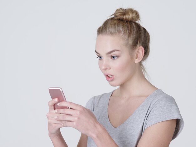 Portrait of a surprised woman with mobile phone in hands  - at studio