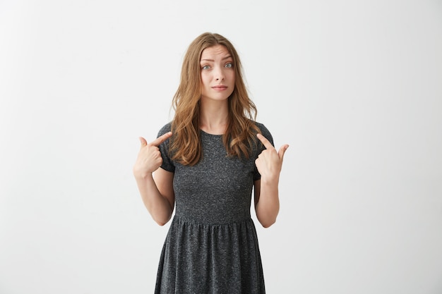 Portrait of surprised young beautiful girl pointing fingers at herself .