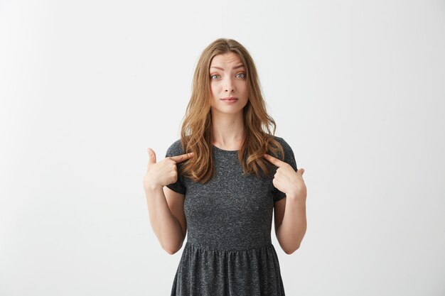 Portrait of surprised young beautiful girl pointing fingers at herself .