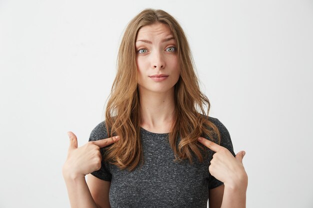 Portrait of surprised young beautiful girl pointing fingers at herself .