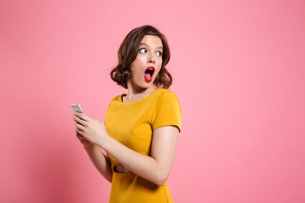 Портрет удивленной молодой женщины, держащей мобильный телефон