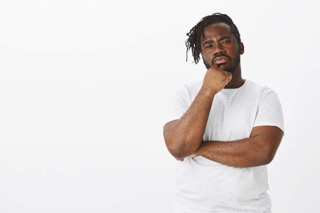 Portrait of suspicious guy with braids posing against the white wall