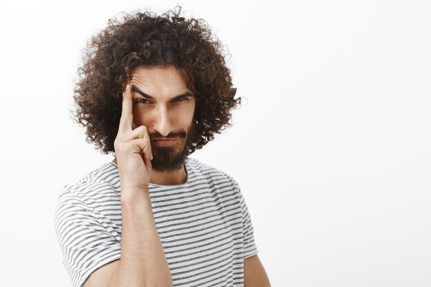 Portrait of suspicious playful bearded man with curly hair, lifting eyebrow with index finger