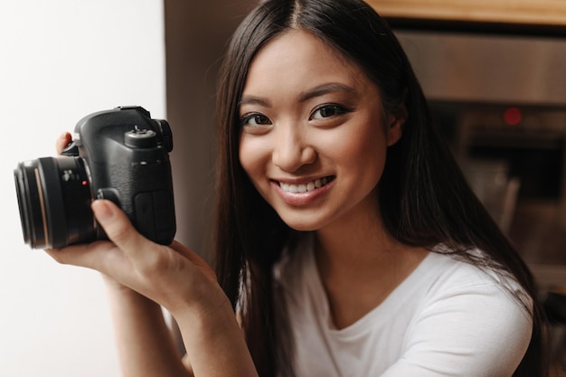 Portrait of tanned girl with dark hair with camera in her hands Woman in white top cute smiles