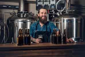 Free photo portrait of tattooed, bearded hipster male manufacturer presenting beer microbrewery.