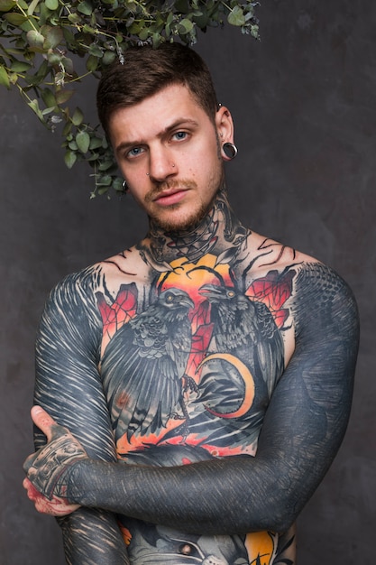 Portrait of a tattooed man with piercing in the ears and nose standing against grey backdrop