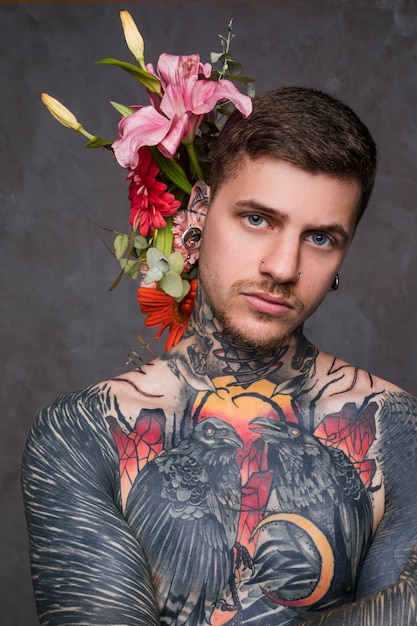 Portrait of a tattooed man with piercing in the ears and nose standing against grey backdrop