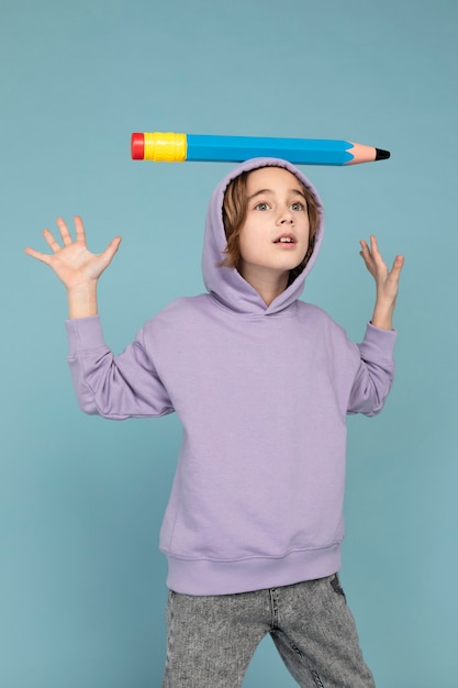 Portrait of teen boy carrying with a big pencil on his head