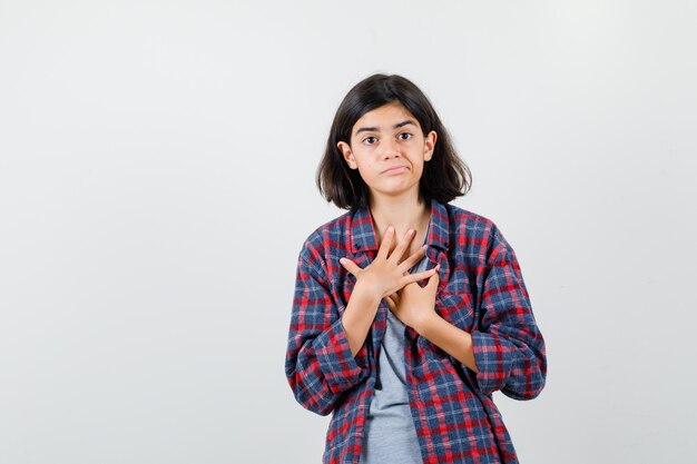 Portrait of teen girl holding hands on chest in casual clothes and looking bewildered front view