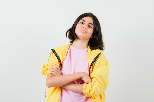 Портрет девочки-подростка, держащей скрещенные руки в футболке, куртке и уверенно выглядящей вид спереди